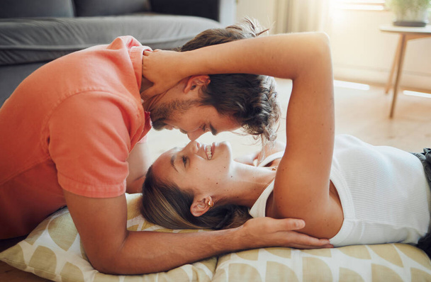 Happy young woman lying on floor while her boyfriend leans over her as they touch noses and looking into each other eyes. Affectionate couple enjoying romantic intimate moment. - Photo, image