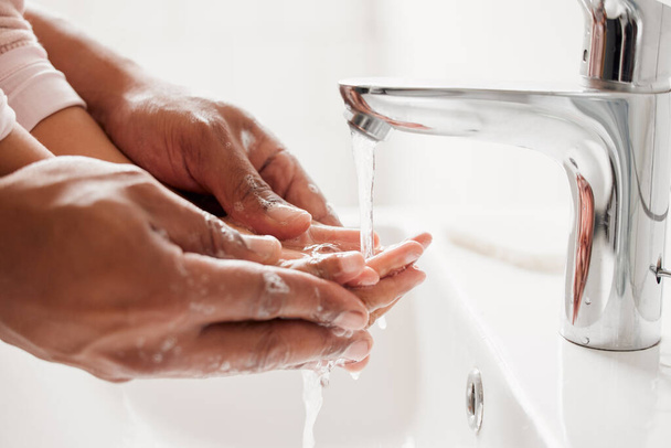 Nieznany mieszana rasa ojciec i córka myją ręce razem w łazience w domu. Nierozpoznawalny samotny Afroamerykanin rodzic uczy córkę higieny. - Zdjęcie, obraz