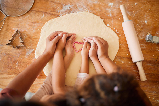 An unknown mother and daughter bonding while baking cookies in a kitchen at home. Unrecognizable mixed race family of two having fun while making shapes in dough. - Foto, Imagen