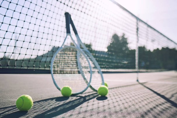 Group of tennis balls and rackets against a net on an empty court in a sports club during the day. Playing tennis is exercise, promotes health, wellness and fitness. Gear and equipment after a game. - Photo, Image