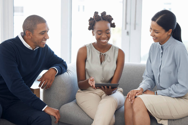 Three happy diverse businesspeople brainstorming and working on a digital tablet together at work. Young african american businesswoman showing her hispanic colleagues an idea on her digital tablet. - Foto, imagen