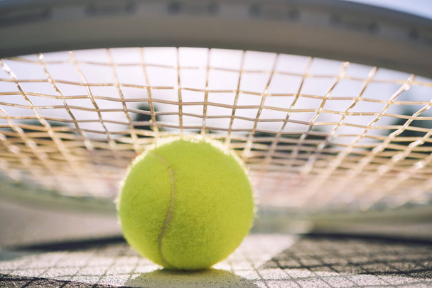 Closeup view of a tennis ball and tennis racket on a court in a sports club during the day. Playing tennis is exercise, promotes health, wellness and fitness. Macro view of tennis gear and equipment. - Fotografie, Obrázek