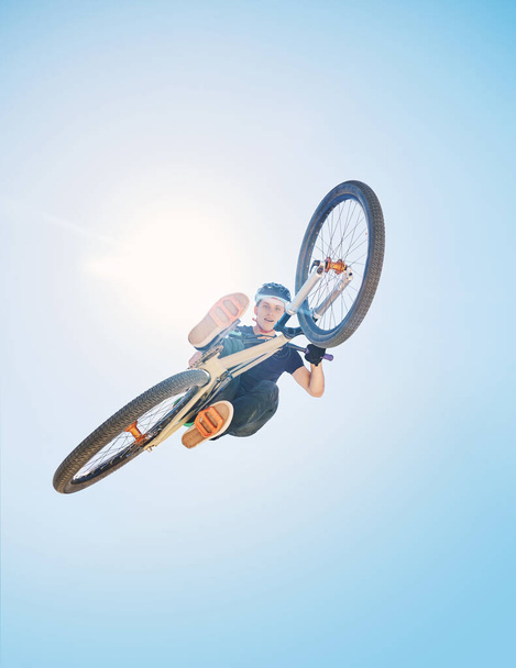 Hombre mostrando sus habilidades de ciclismo mientras pedalea en una bicicleta fuera. Un adicto a la adrenalina practicando un salto de tierra al aire libre. Hombre usando un casco haciendo trucos con una bicicleta. Flotando, apasionado y libre. - Foto, Imagen