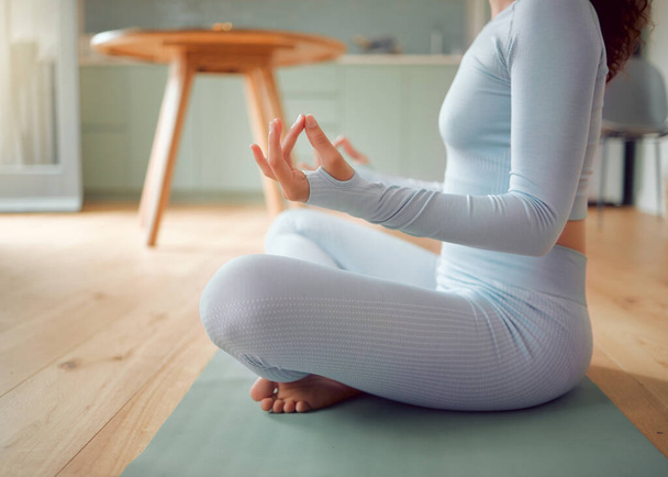 Zbliżenie młoda mieszana rasa kobieta medytująca w pozycji asana podczas praktykowania jogi w domu. Nierozpoznawalna kobieta ćwiczy swoje ciało i umysł, odnajdując wewnętrzny spokój, równowagę i przejrzystość. - Zdjęcie, obraz