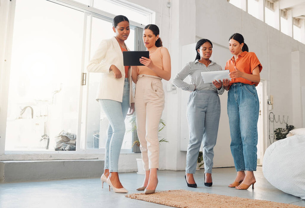 Group of businesswomen talking and using a digital tablet and report together at work. Serious businesspeople talking and planning while standing in an office. - 写真・画像