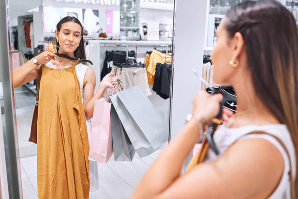 Mooie jonge vrouw kijkt naar kleding in een spiegel in een warenhuis. Kleding passen tijdens het winkelen voor modeverkoop. Retail therapie is precies wat ze nodig had. De klant heeft altijd gelijk.. - Foto, afbeelding