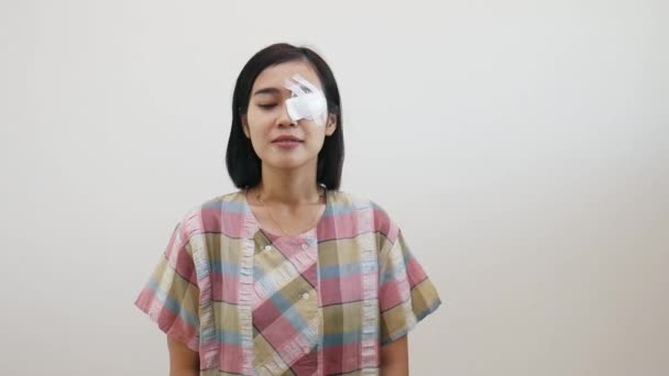 Aasialainen nainen seisoo silmien suojelija samalla näyttää dont kuten savua ele. Hoito post silmäleikkaus tai kaihileikkaus käsite. Eristetty valkoisella seinällä. - Materiaali, video