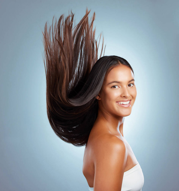 Portrait of a hispanic brunette woman with long lush beautiful hair smiling and posing against a grey studio background. Mixed race female standing showing her beautiful healthy hair. - Photo, Image