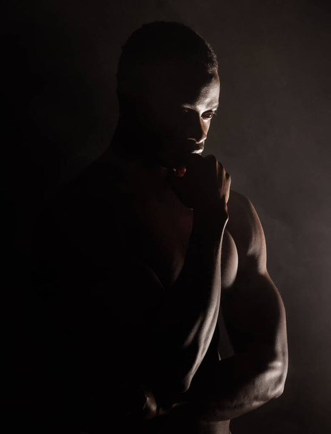 Hezký, svalnatý mladý africký Američan z ateliéru na tmavém pozadí. Chlapský atlet, který vypadá zamyšleně izolovaný na černém. Cvičení těla a mysli. Otázka duševního zdraví. - Fotografie, Obrázek
