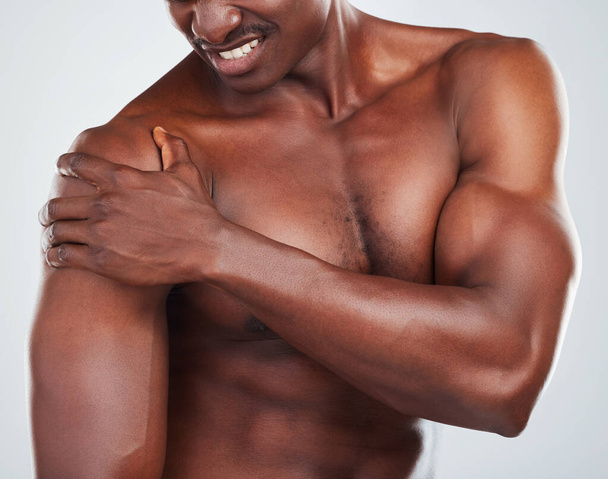 One unknown muscular fitness model experiencing shoulder pain from an injury while exercising. Black topless athlete holding his arm in pain while isolated on grey copyspace in a studio. - Foto, Imagem
