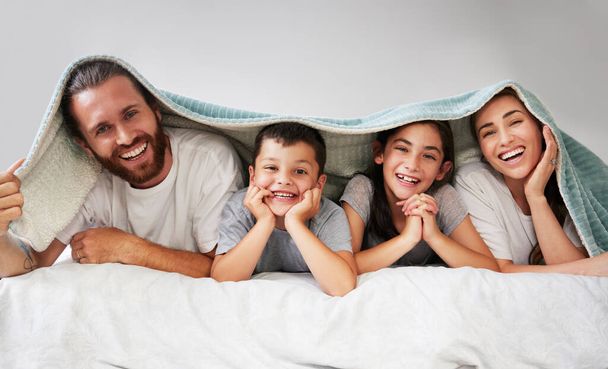 Portret van een gelukkige blanke familie van vier die samen op bed liggen met een sherpa deken over hun hoofd. Zorgeloze ouders die dit weekend vrije tijd doorbrengen met hun dochter en zoon. Lachen. - Foto, afbeelding
