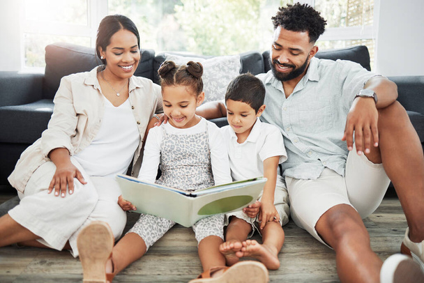 Mieszana rodzina rasowa czyta razem książkę na podłodze w domu. Latynoska matka i ojciec uczą syna i córkę czytać. Brat i siostra uczą się czytać z rodzicami. - Zdjęcie, obraz