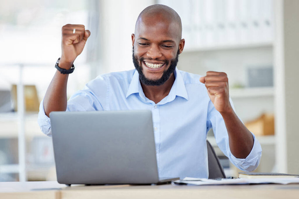 Young happy african american businessman cheering with joy and working on a laptop in an office at work alone. One cheerful male business professional cheering with his fists and using a computer - Fotoğraf, Görsel