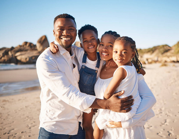Portrait of a happy african american family with two children standing together on the beach. Loving mother and father carrying their daughter and son while spending time together on vacation. - Photo, image