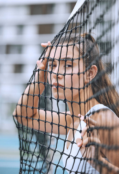 Close up of a female athlete leaning against a tennis net. Young hispanic tennis player posing on a tennis court. - Foto, imagen