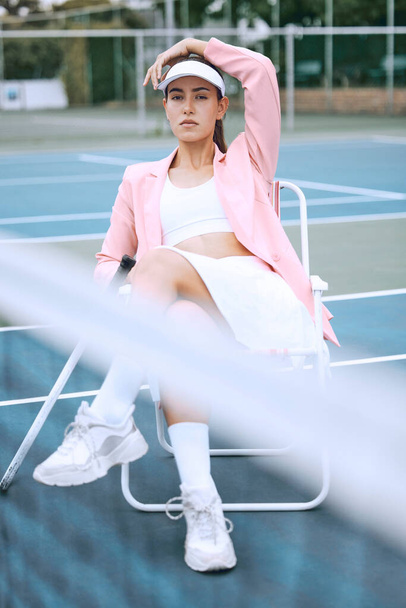 Trendy mladý tenista v růžové bundě, zatímco sedí na židli na tenisovém kurtu. Mladá hispánská sportovkyně sedící s tenisovou raketou po zápase. - Fotografie, Obrázek