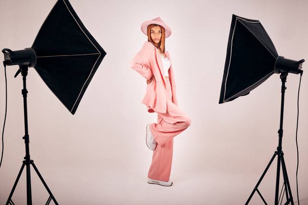 Serious young mixed race woman posing in trendy fashionable clothing while standing in a studio shoot. Confident hispanic woman posing in pink clothes in a studio with bright lights. - Zdjęcie, obraz