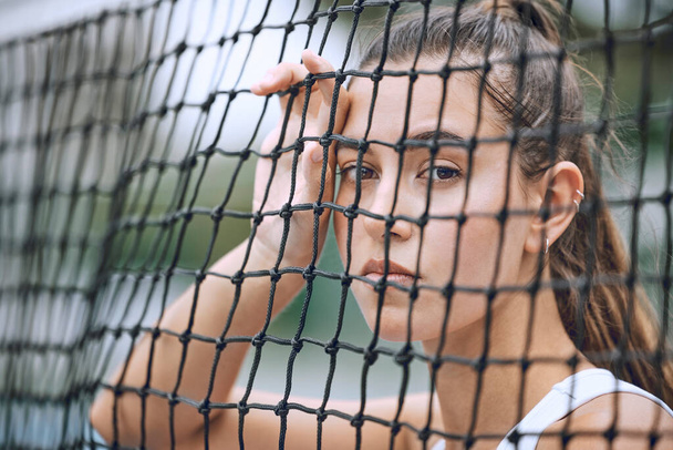 Primo piano di un'atleta donna appoggiata a una rete da tennis. Giovane tennista ispanico in posa su un campo da tennis. - Foto, immagini