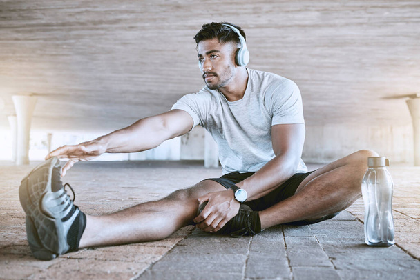 Fit young man stretching his legs while exercising outdoors. Handsome indian man touching his toes to warmup for a run. - Φωτογραφία, εικόνα