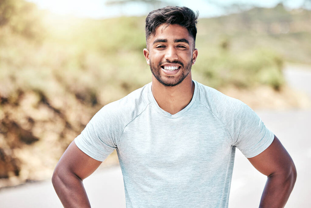 Portrait of happy young mixed race man getting ready to workout. Young hispanic man smiling and standing with his hands on his hips outside. Getting fitter with each day of running and exercise. - Photo, image