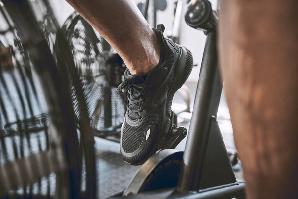 Egy fitt férfi lába biciklizik a tornateremben. Edző kerékpározás sportcipőben a tornateremben. A testépítő tornateremben biciklizett. Viselje a megfelelő cipőt, amikor a tornateremben gyakorol. Erős lábak építése biciklin. - Fotó, kép