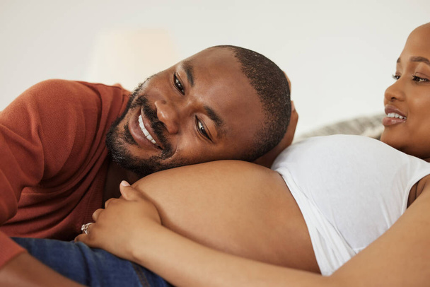 Feliz joven afroamericano padre para estar escuchando a sus esposas embarazadas vientre y sonriendo. Joven poniendo su cabeza contra su vientre esposas expectantes escuchando para el movimiento. - Foto, Imagen