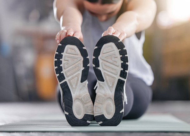 Closeup of one active caucasian woman touching her feet and stretching legs for warmup to prevent injury while exercising in a gym. Bottom sole of shoes of female athlete preparing for training - Zdjęcie, obraz