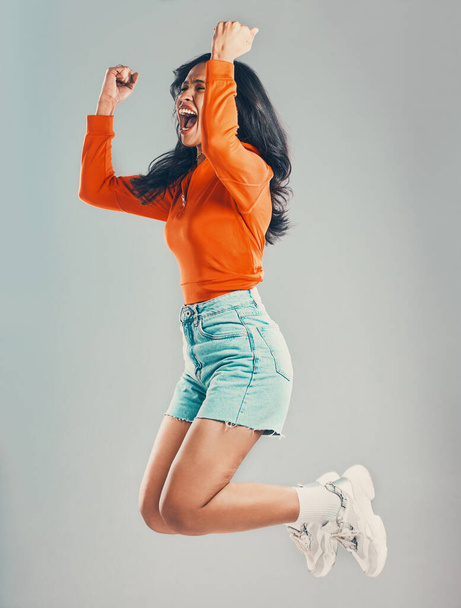 Full length mixed race woman jumping and isolated against grey studio background with copyspace. Young hispanic celebrating success alone midair. Excited, cheering model making fists with hand gesture - Foto, Imagen