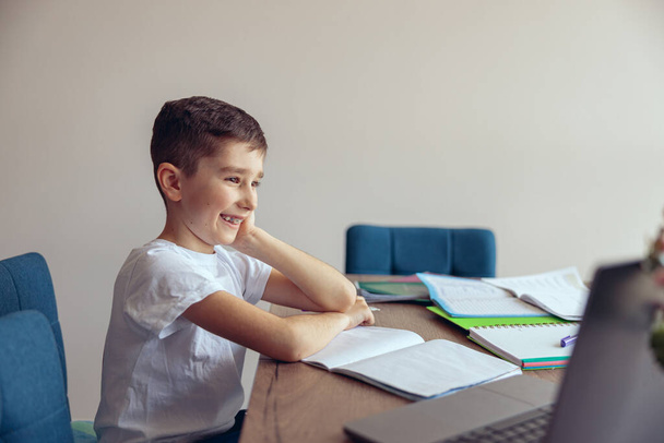 Portrait de joyeux écolier joyeux avec bretelles regarder leçon en ligne sur ordinateur portable et souriant. - Photo, image