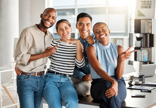 Portrait of a group of diverse cheerful businesspeople making hand gestures and spending time in an office together at work. Joyful business professionals smiling while bonding at work. - 写真・画像
