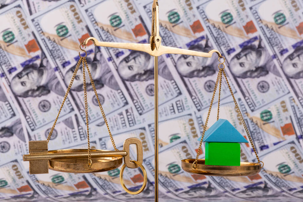A golden key on both sides of the scale and a symbolic house on the other side of the scale against the background of US $100 bills - Photo, image