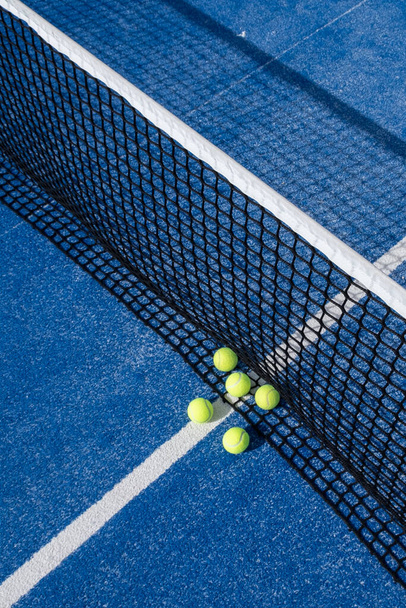 A closeup of several paddle tennis balls by the net on a blue paddle tennis court - Foto, Imagem