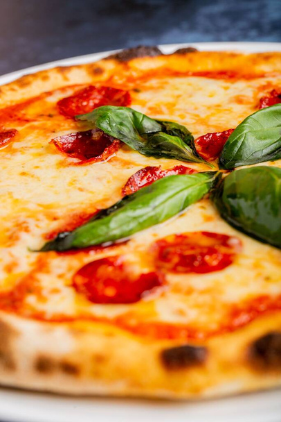 Fresh tasty pepperoni pizza with basil leaves on the table - Foto, afbeelding