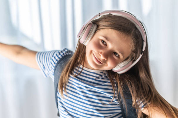 Cute baby listens to music through wireless headphones, enjoys tunes and dances. - Фото, изображение