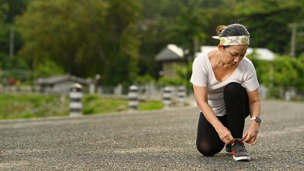 Frau mittleren Alters bindet Schnürsenkel, macht sich bereit zum Joggen im Freien. Gesunder Lebensstil. - Foto, Bild