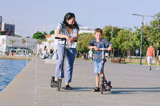 Gelukkige familie levensstijl en vakantie concept. Moeder, kleine jongen, meisje, paardrijden scooters, wandelen in de oude stad, straat. IJs. Lachen op een zonnige zomerdag. Veel plezier. - Foto, afbeelding