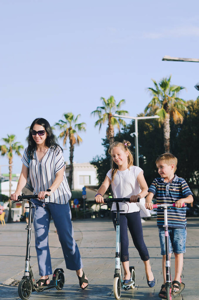 Felice stile di vita familiare e concetto di vacanza. Mamma, bambino, ragazza, cavalcando scooter, passeggiando nel centro storico, per strada. Gelato. Ridere in una giornata di sole estivo. Divertirsi - Foto, immagini