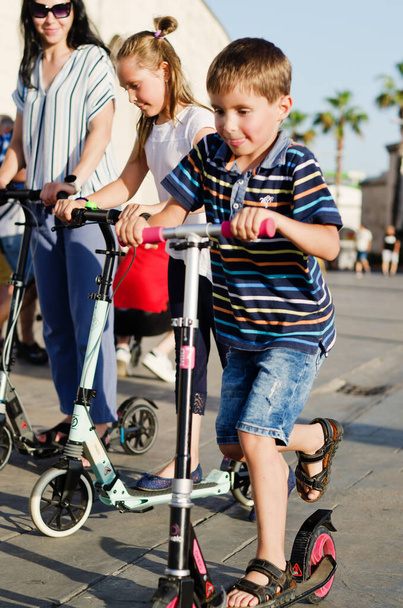 Felice stile di vita familiare e concetto di vacanza. Mamma, bambino, ragazza, cavalcando scooter, passeggiando nel centro storico, per strada. Gelato. Ridere in una giornata di sole estivo. Divertirsi - Foto, immagini