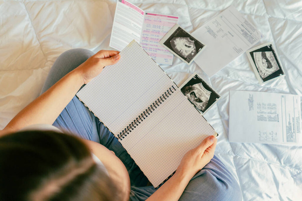 妊婦リスト。妊娠中の母親がメモ帳を持ってる。妊娠中の女性は赤ん坊のチェックリストを書く。妊娠、出産、医療の概念 - 写真・画像