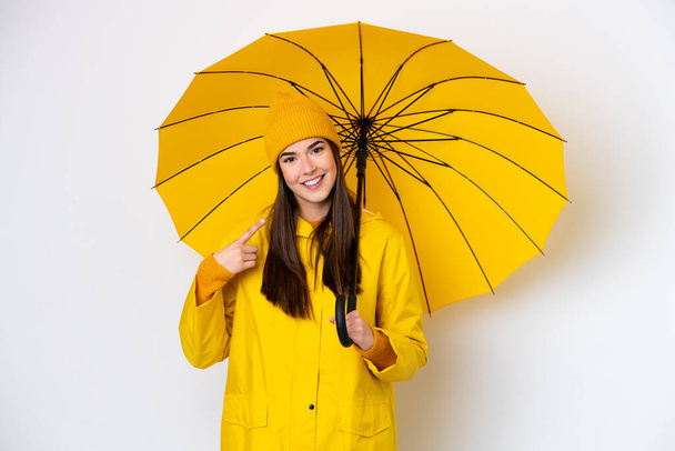 Young Brazilian woman with rainproof coat and umbrella isolated on white background giving a thumbs up gesture - 写真・画像