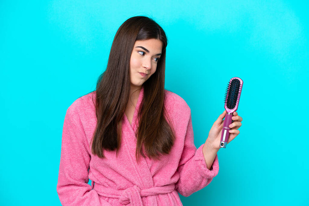 Young Brazilian woman holding hairbrush isolated on blue background with sad expression - Photo, Image
