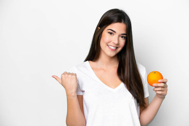 Junge Brasilianerin mit einer orangefarbenen Isolierung auf weißem Hintergrund, die zur Seite zeigt, um ein Produkt zu präsentieren - Foto, Bild
