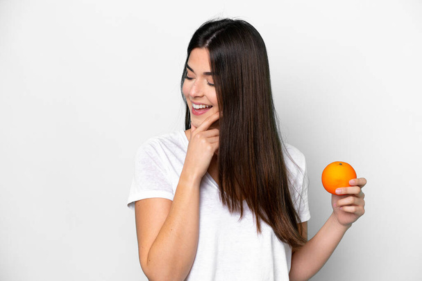 白い背景に孤立したオレンジを持っている若いブラジル人女性はアイデアと見ている側を考え - 写真・画像