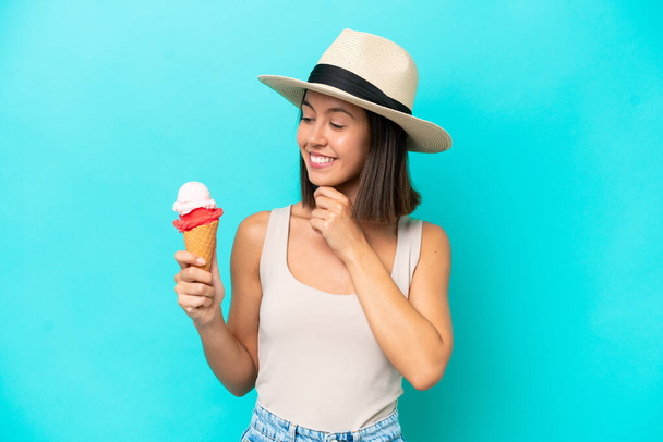 Young caucasian woman holding an ice cream isolated on blue background and looking up - Zdjęcie, obraz