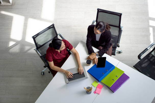 Дві азіатські бізнес-леді зустрічаються в сучасному офісі з ноутбуком, планшетом, папкою документів і кавою на столі. Концепція корпоративної ділової команди. Вид зверху
 - Фото, зображення