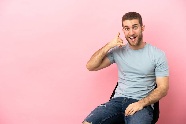 Young man sitting on a chair over isolated pink background making phone gesture. Call me back sign - Foto, Bild
