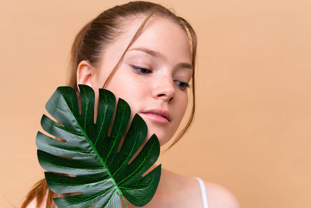 Young caucasian girl isolated on beige background holding a palm leaf. Close up portrait - Fotografie, Obrázek