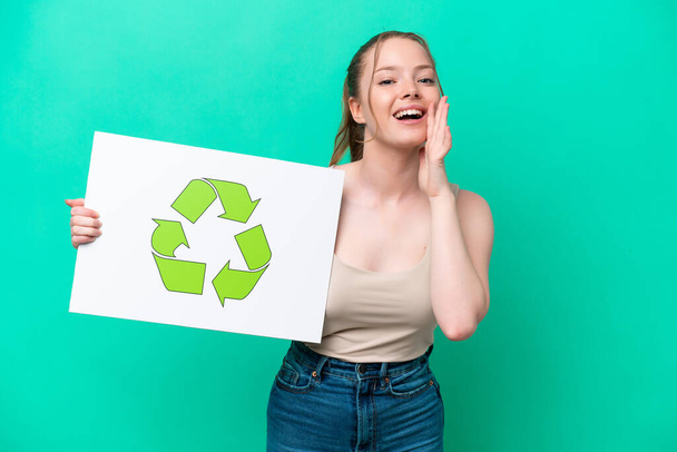 Young caucasian woman isolated on green background holding a placard with recycle icon and shouting - Foto, Imagen
