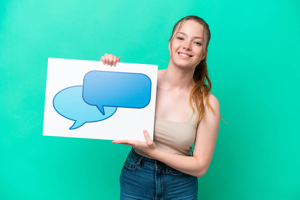 Young caucasian woman isolated on green background holding a placard with speech bubble icon with happy expression - Photo, Image