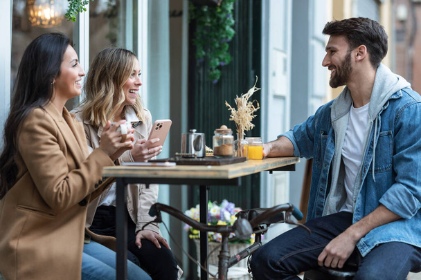 Shot of group of cool friends sharing a brunch together while talking and using the smartphone on the healthy coffee shop terrace. - Foto, Imagem